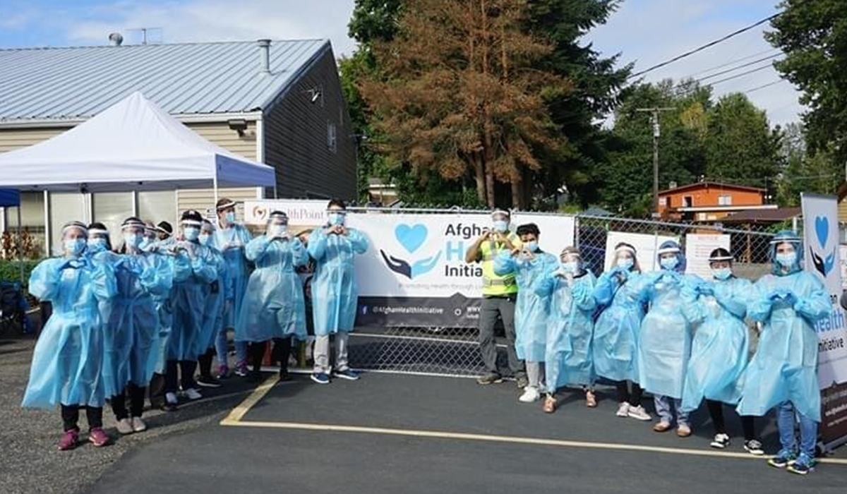 AHI Team in scrubs, masks and face shields pose in front of banner at mass vaccination event